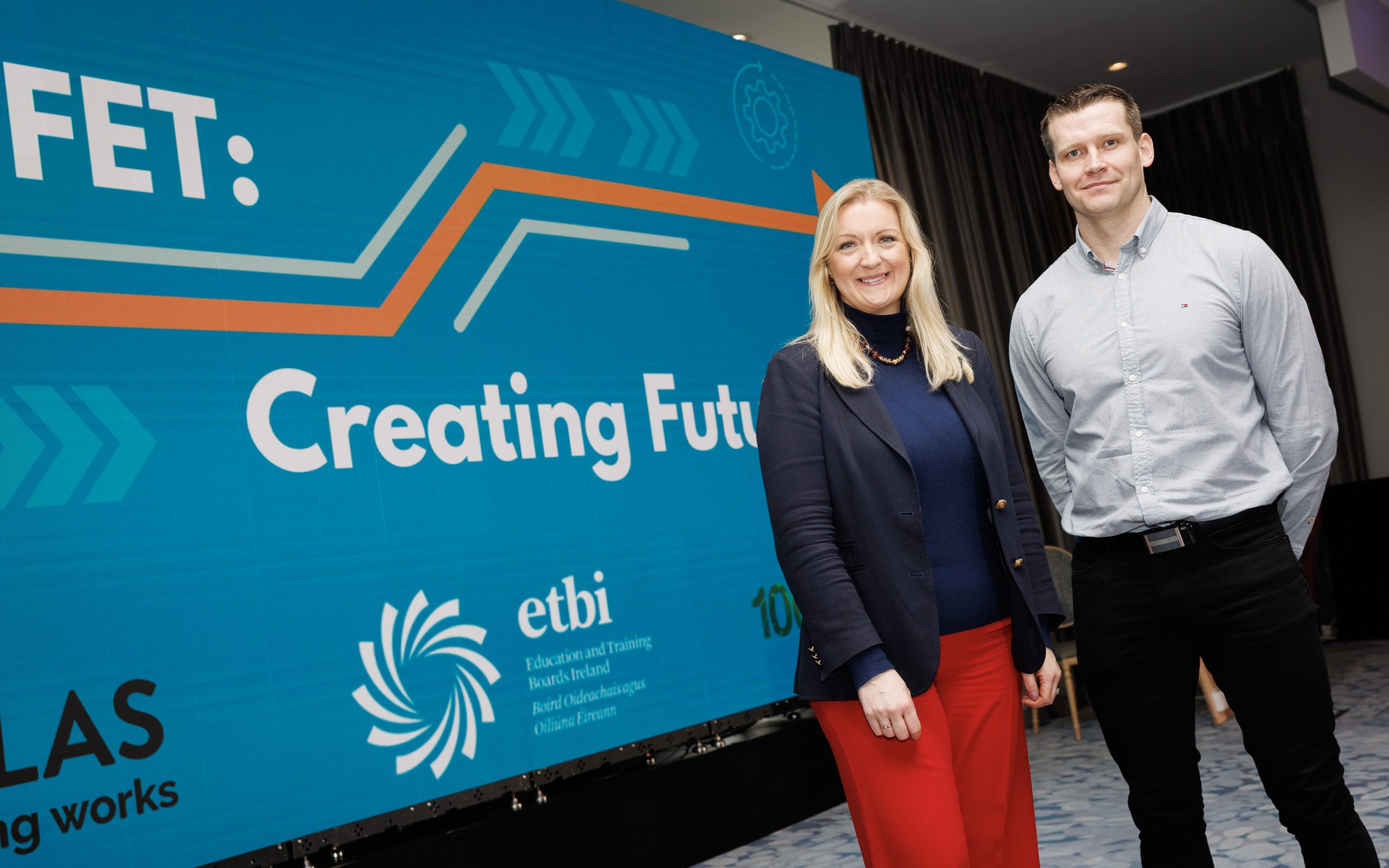 Man and woman posing in front of large screen